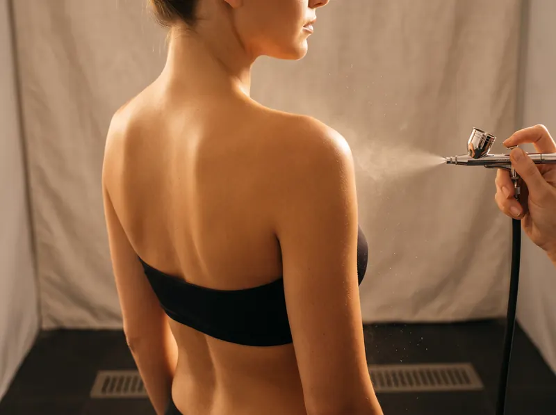 Application d'un tanning spray par brumisation sur le dos d'une cliente